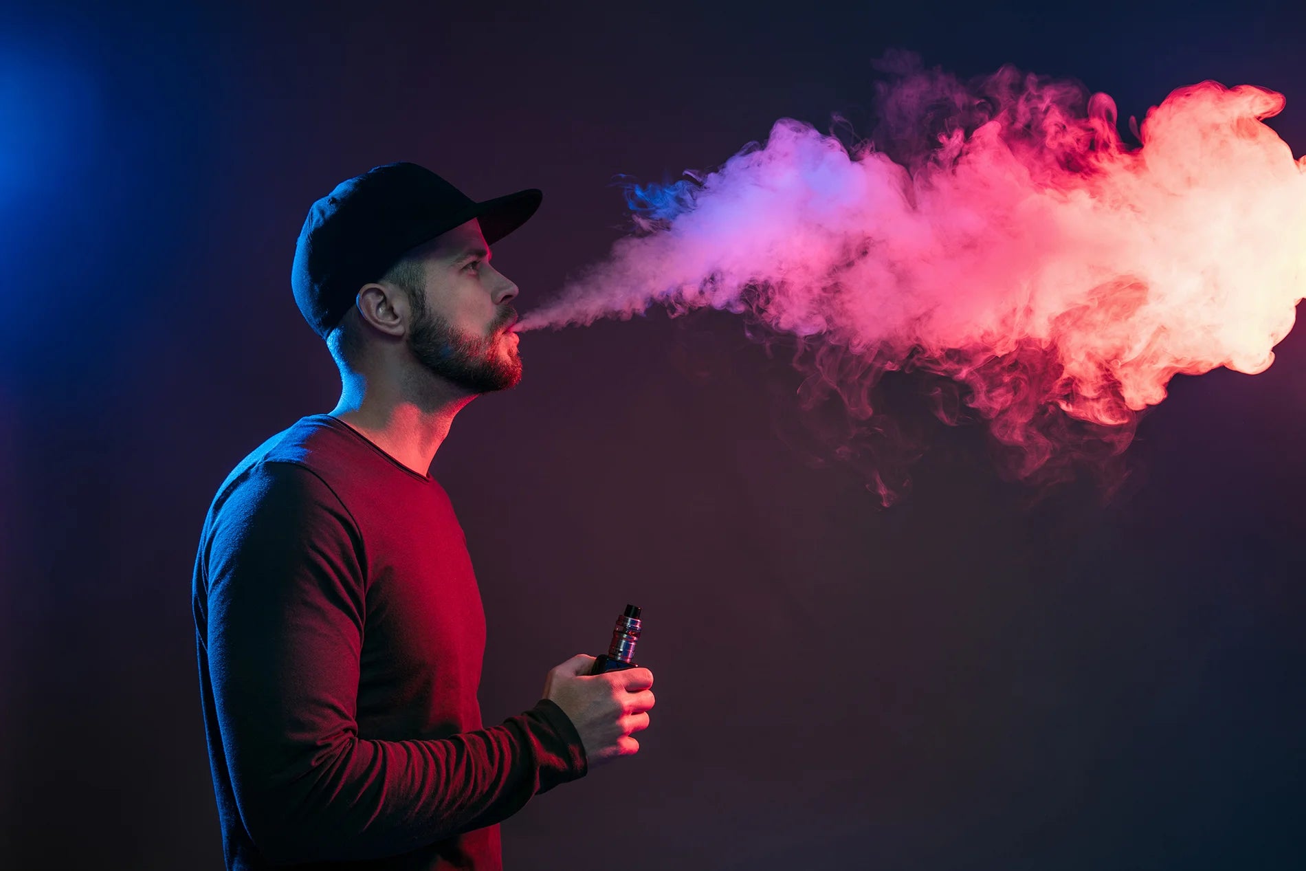 Man exhaling colorful smoke from an iluma device against a dark background